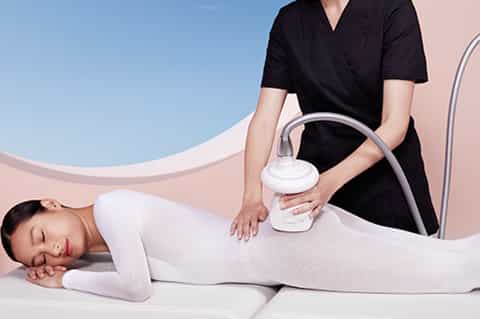 Spa technician using ultrasonic device for body treatment on client lying on massage table
