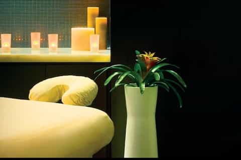 Luxury spa bathroom with yellow curved furniture, decorative candles in tiled niche, green plant accent, and minimalist design