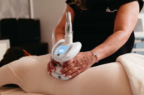 Spa therapist performing ultrasound body treatment on client's leg with handheld device