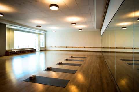 Fitness studio with mirror wall, yoga mats, wooden flooring, and bright natural lighting