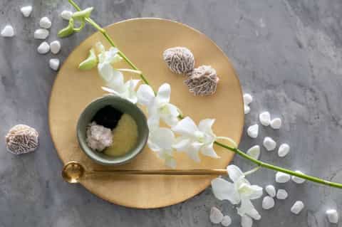 Spa styling flat lay with gold dish, white orchid flowers, sea salt, and natural spa accessories