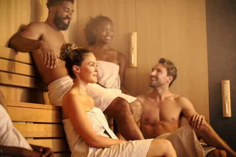 Groups of people relaxing in wooden sauna with warm ambient lighting and bench seating