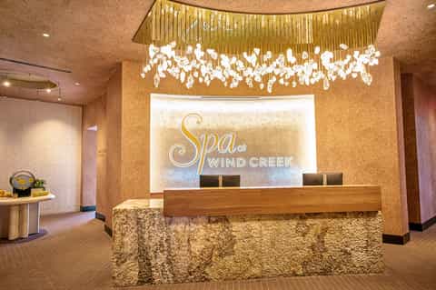 Elegant spa reception desk with brass chandelier and stone accent wall at Wind Creek