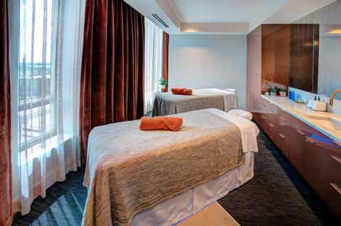 Spa treatment room with two massage beds, vanity, ocean view windows, and warm lighting