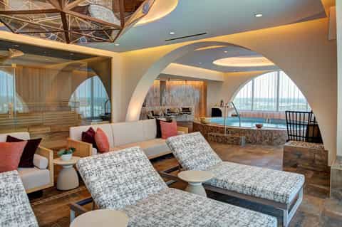 Luxury spa lounge with curved architecture, loungers, sauna, hot tub, and panoramic windows