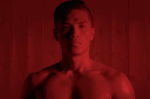 Shirtless man standing against deep red paneled wall in dramatic moody lighting