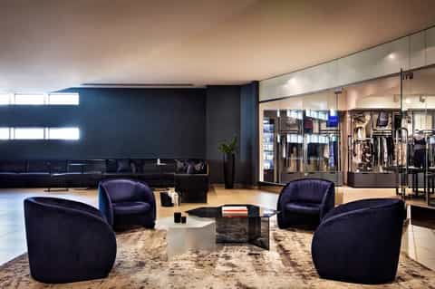 Contemporary hotel lobby with navy curved chairs, dark walls, glass retail storefront, and wood flooring
