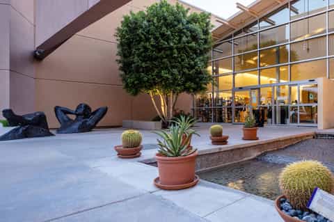 Modern courtyard with art sculpture, potted plants, and glass-fronted building entrance