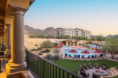 Desert resort pool area with red umbrellas, lounge seating, and mountain backdrop at golden hour