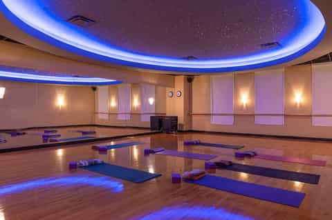 Yoga studio with blue LED ceiling lights, wooden floor, yoga mats, and mirrored walls