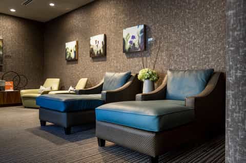 Contemporary lounge with dark woven chairs, blue cushions, textured wallpaper, and framed artwork