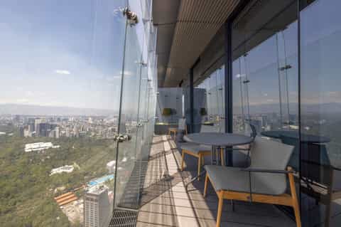 High-rise balcony with glass railings overlooking city skyline and park landscape