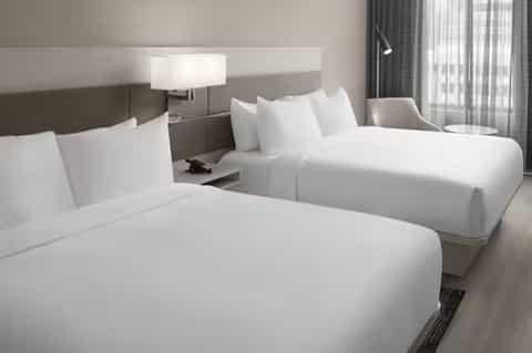 Modern hotel guest room with two queen beds, neutral tones, and large windows