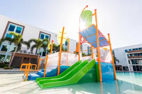 Colorful children's playground with green slide, bright orange frame, and modern residential building