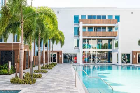 Contemporary resort courtyard with modern white building, wooden railings, palm trees, and lap pool