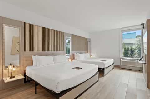 Modern hotel room with two queen beds, wooden accent wall, and contemporary furnishings