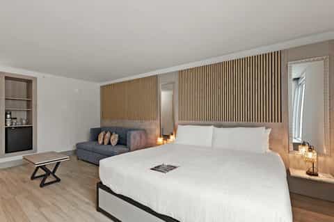 Modern hotel room with king bed, sofa, wooden wall panels, and contemporary minimalist design