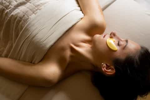 Woman relaxing on bed during spa treatment with yellow eye pads