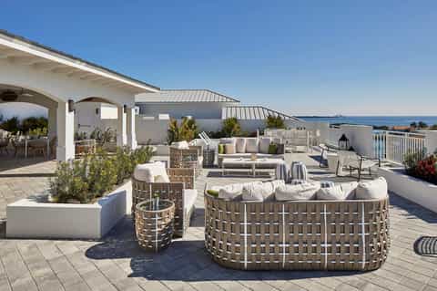 Rooftop terrace with woven lounge seating, ocean views, and white architectural elements