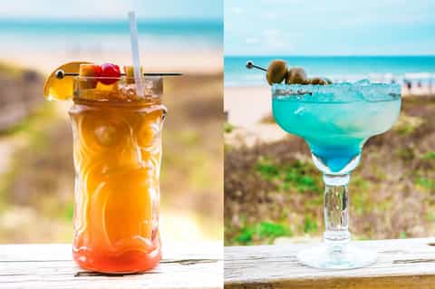 Two colorful cocktails on beach with ocean and sand dunes in background