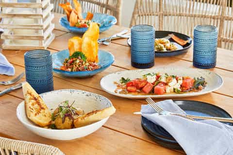 Fine dining table setting with plated seafood dishes, blue glasses, and coastal view backdrop