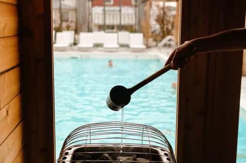 Hand pouring water into bucket overlooking resort swimming pool and seating area