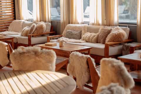 Ship's lounge with cream seating, fluffy pillows, wooden frames, and ocean view windows