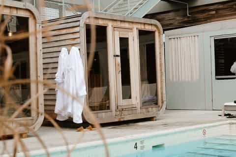 Wooden spa pod cabanas beside an indoor lap pool with white towels and modern resort facility design