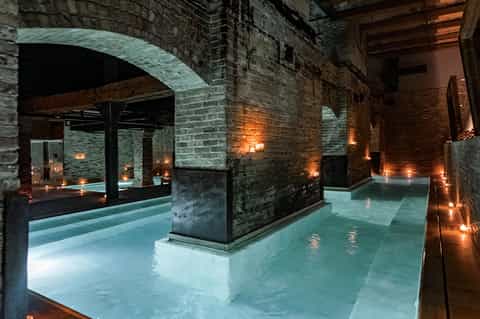 Underground spa or pool area with brick arches, ambient lighting, and illuminated water features
