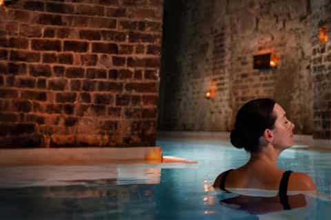 Woman enjoying geothermal hot spring pool with stone walls and golden ambient lighting