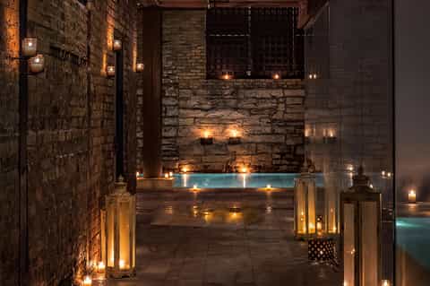Luxurious spa courtyard with illuminated indoor pool surrounded by stone walls and ambient candlelight