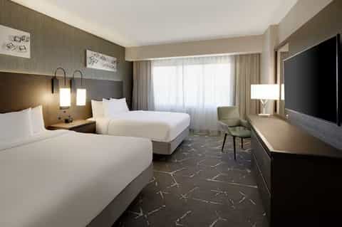 Hotel guestroom with two queen beds, neutral colors, flat-screen TV, and modern furnishings