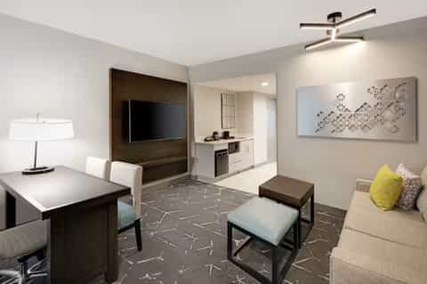 Modern hotel suite with TV, kitchenette, seating area, and contemporary furnishings