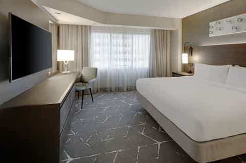 Contemporary hotel room with queen bed, flat-screen TV, desk, and floor-to-ceiling windows