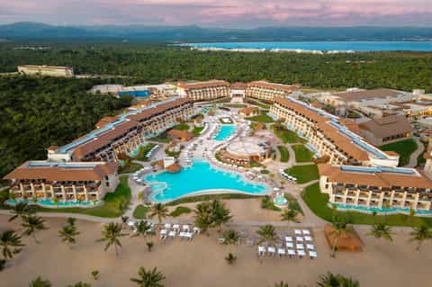 Aerial view of large beachfront resort complex with pools, multi-story buildings, and jungle backdrop