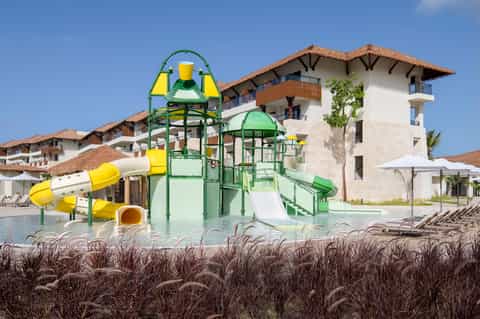 All-inclusive resort with colorful water slides, white building, thatched roof, and beachfront setting