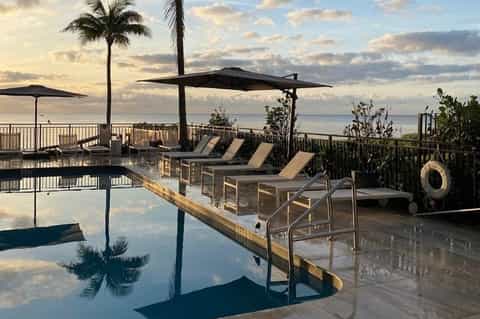 Oceanfront resort infinity pool at sunset with lounge chairs, umbrellas, and tropical coastal views
