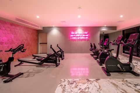 Modern fitness center with pink ceiling, neon signage, and rows of black exercise bikes