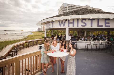 Beachfront bar pavilion with wooden deck, people socializing, and ocean views