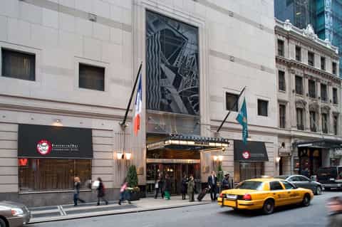 Urban hotel entrance on city street with yellow taxi, flags, and pedestrians