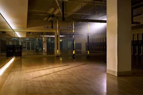Empty fitness studio with mirrors, wooden floors, suspension trainers, and professional gym equipment
