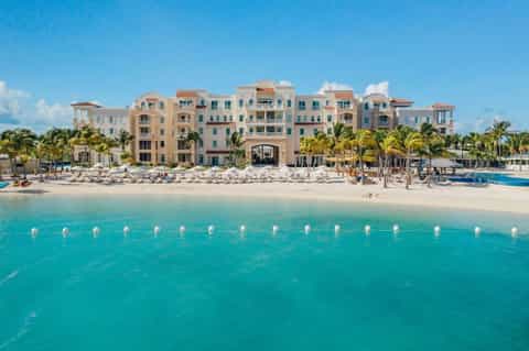 Colorful beachfront resort with multi-story pastel buildings, white sand beach, turquoise water, and palm trees