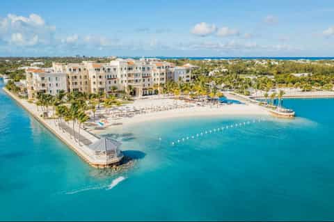 Aerial view of beachfront resort with turquoise water, white buildings, palm trees, and pristine sandy beach