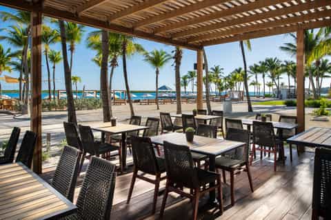 Beachfront dining pavilion with wooden pergola, palm trees, and ocean view through columns