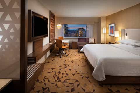 Hotel room with king beds, city night views, desk, and warm interior lighting