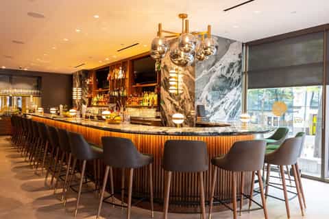 Upscale bar with curved marble counter, bronze pendant lights, and city views through windows