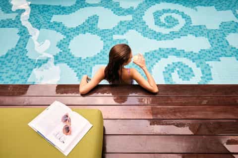 Woman in swimming pool holding a drink with colorful mosaic tile design visible