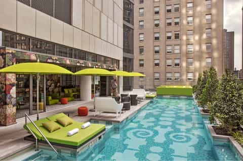 Urban rooftop pool with lime green lounge chair, modern building, and decorative water tile pattern