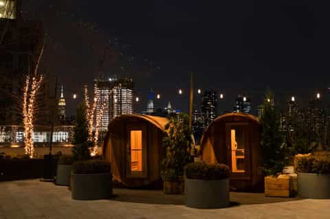 Rooftop wooden sauna pods with city skyline at night and illuminated trees