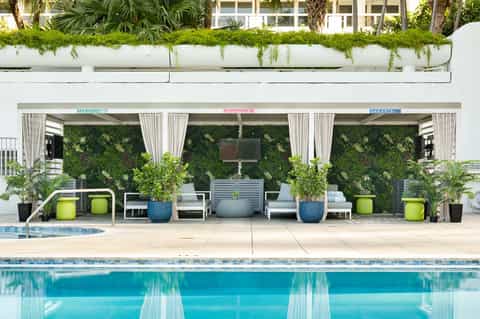 Modern poolside cabanas with green living walls, white curtains, and lounge seating area